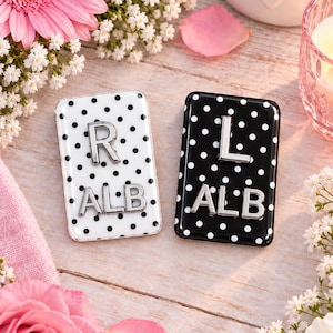 May include: Two rectangular metal cases with a black polka dot pattern on a white background and a white polka dot pattern on a black background. Each case features raised silver-toned letters with R and ALB on one, and L and ALB on the other.