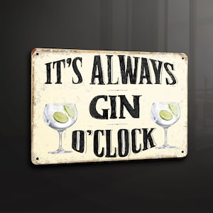 Puede incluir: Un letrero de metal blanco con texto negro que dice "It's Always Gin O'Clock". El letrero presenta dos ilustraciones de gin tonic con rodajas de lima.