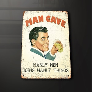 Puede incluir: Un letrero de metal de estilo vintage con un aspecto oxidado y desgastado. Presenta a un hombre de dibujos animados con traje sosteniendo un vaso de líquido y el texto "Man Cave Manly Men Doing Manly Things".