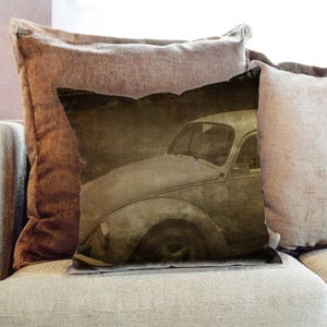 Puede incluir: Una almohada de tiro marrón y beige con una imagen vintage de un coche clásico. El coche es de color marrón claro y tiene una forma redondeada. La almohada está hecha de una tela suave y texturizada.
