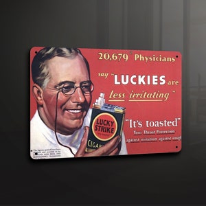 Puede incluir: Letrero metálico vintage con fondo rojo que presenta una ilustración de un hombre sonriente con gafas. El letrero promociona los cigarrillos "LUCKIES", afirmando que son "menos irritantes". También se muestra el texto "It's toasted".