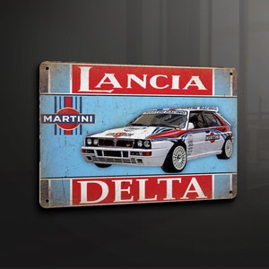 Puede incluir: Una placa de metal de estilo vintage con un coche de rally Lancia Delta blanco con la decoración de Martini Racing. La placa tiene un fondo azul con detalles rojos y blancos y el texto "Lancia Delta" en letras rojas.