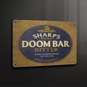 May include: A vintage-style metal sign advertising Sharp's Brewery Doom Bar Bitter. The sign is yellowed and worn, with a blue oval featuring the brewery's logo and the text "Sharp's Brewery Doom Bar Bitter". The sign also includes the text "Cask Conditioned Alc 4.0% Vol Rock, Cornwall".