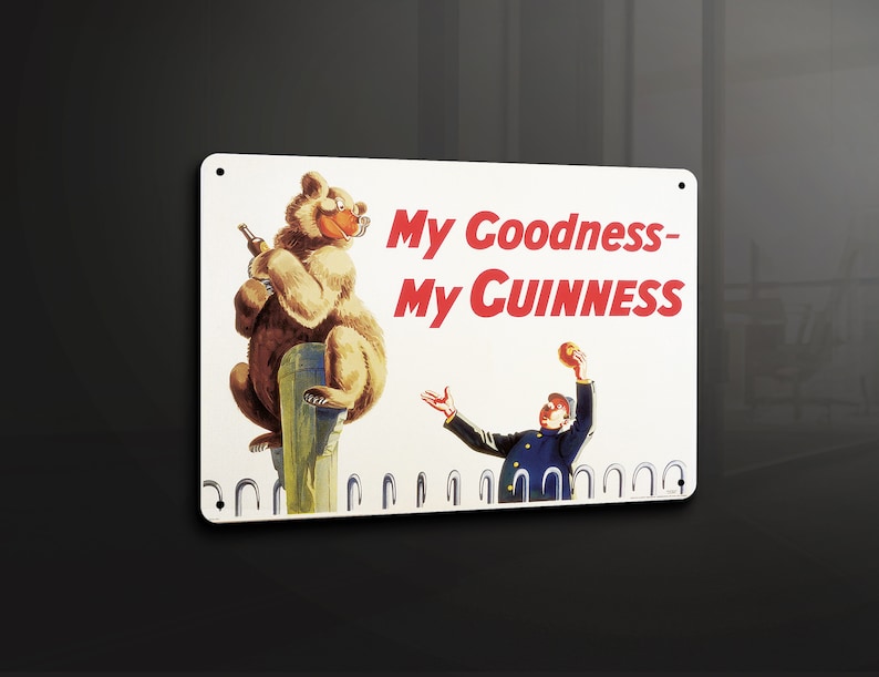 May include: A white metal sign with a brown bear holding a bottle of Guinness and the text "My Goodness - My Guinness". A man in a blue uniform is throwing a ball in the air.