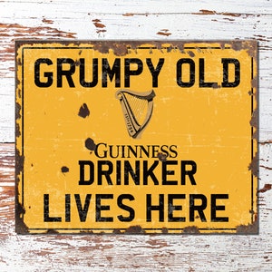 Puede incluir: Un letrero de metal amarillo con un aspecto desgastado y oxidado. El letrero dice "GRUMPY OLD GUINNESS DRINKER LIVES HERE" con un logotipo negro de la arpa de Guinness.