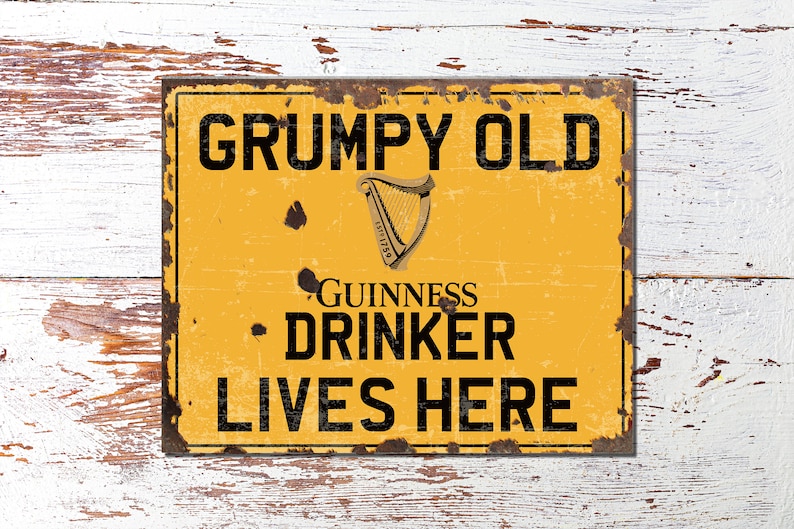 May include: A yellow metal sign with a distressed, rusty look. The sign reads "GRUMPY OLD GUINNESS DRINKER LIVES HERE" with a black Guinness harp logo.