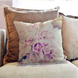Puede incluir: Una almohada floral rosa y blanca con estética vintage. La almohada presenta un primer plano de un ramo de flores rosas con un aspecto suave y descolorido.