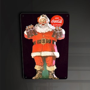 Puede incluir: Un letrero de metal vintage de Coca-Cola con una ilustración de Papá Noel sosteniendo botellas de Coca-Cola. El letrero tiene un logotipo rojo de Coca-Cola con el texto "Sirva Coca-Cola Signo de buen gusto".