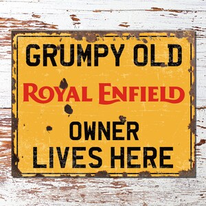 Puede incluir: Un letrero de metal amarillo con texto negro y rojo que dice "Grumpy Old Royal Enfield Owner Lives Here". El letrero tiene un aspecto desgastado y vintage.