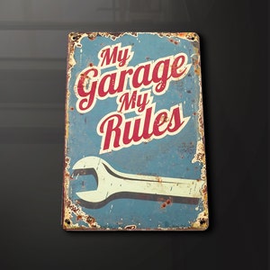 Puede incluir: Un letrero de metal azul y rojo con el texto "My Garage My Rules" y una llave inglesa debajo. El letrero tiene un aspecto desgastado y oxidado.