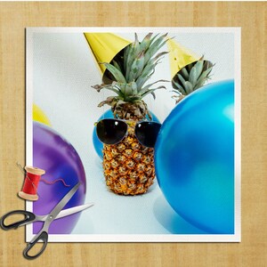 Puede incluir: Imagen caprichosa de una piña con gafas de sol y un gorro de fiesta, rodeada de globos azules y morados. Una bobina de hilo rojo y unas tijeras están en primer plano. La piña es el punto focal, sugiriendo un tema divertido y festivo.