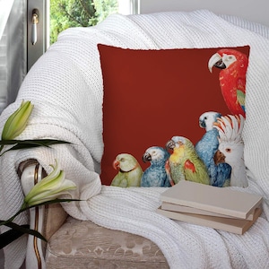 Puede incluir: Una almohada de color rojo, marrón, verde, azul y blanco con un patrón de loros coloridos. La almohada está sentada en una manta blanca en una silla.