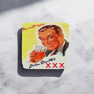 Peut inclure: Une publicité vintage pour la bière John Smith's XXX avec un homme souriant tenant un verre de bière. La publicité a un fond jaune avec le texte "You will enjoy..." et le nom de la marque "John Smith's XXX" en rouge.