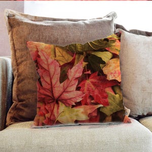 Puede incluir: Una almohada con una imagen de primer plano de hojas de otoño coloridas en tonos de rojo, naranja, amarillo y verde.