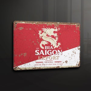 Puede incluir: Un letrero de metal rojo, blanco y dorado con un aspecto desgastado. Presenta un dragón rojo y el texto "Bia Saigon Export - Original Premium Quality Beer from Vietnam - Est. 1875".