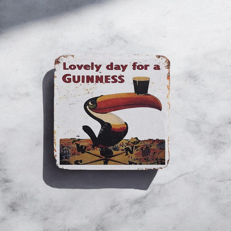 Puede incluir: Un letrero de metal blanco con un tuc&aacute;n sosteniendo un vaso de Guinness. El letrero dice "Lovely day for a GUINNESS".