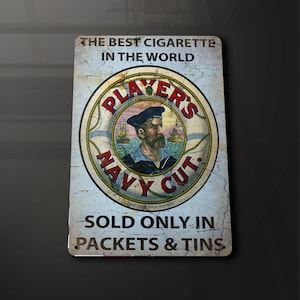 Puede incluir: Un letrero metálico vintage con el texto "THE BEST CIGARETTE IN THE WORLD". El letrero presenta un gráfico circular con un marinero y las palabras "PLAYER'S NAVY CUT". También se lee "SOLD ONLY IN PACKETS & TINS".