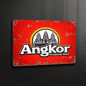 Puede incluir: Un letrero de metal rojo oxidado con un contorno blanco y las palabras "Angkor Premium Beer" en blanco. El letrero presenta una ilustración en blanco y negro del complejo del templo de Angkor Wat.