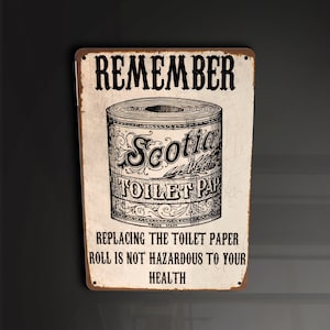 Puede incluir: Un letrero metálico rectangular con un diseño vintage. El letrero presenta la palabra "REMEMBER" en la parte superior, con una ilustración de un rollo de papel higiénico y el texto "Scotia TOILET PAPER". El texto inferior dice "REPLACING THE TOILET PAPER ROLL IS NOT HAZARDOUS TO YOUR HEALTH".