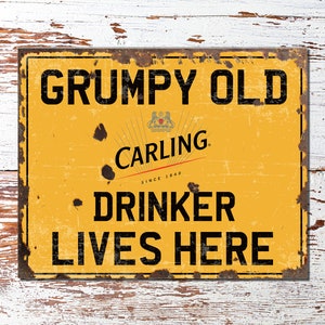 Puede incluir: Un letrero de metal amarillo con un aspecto desgastado y oxidado. El letrero dice "GRUMPY OLD CARLING DRINKER LIVES HERE". El logotipo de Carling es una corona con un león y las palabras "SINCE 1940".