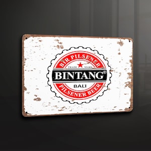 Puede incluir: Un letrero de metal de estilo vintage con fondo blanco y un logotipo rojo y negro para la cerveza Bintang Bali Pilsener. El logotipo presenta una estrella y el texto "Bir Pilsener Trade Mark Bintang Bali Pilsener Beer".