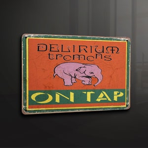 Puede incluir: Un letrero metálico rectangular con un acabado envejecido. El letrero presenta las palabras "DELIRIUM tremens" en negro, con una ilustración de un elefante rosa y las palabras "ON TAP" en amarillo. El fondo es naranja y verde.