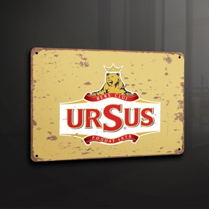 Puede incluir: Un letrero de metal de estilo vintage con un fondo amarillento y un logotipo rojo y blanco para Ursus Bere Cluj. El logotipo presenta un oso con una corona y el texto "Ursus" en una fuente roja y negrita. El letrero también incluye el texto "Bere Cluj" y "Fondat 1878".