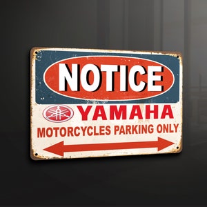 Puede incluir: Un letrero metálico rectangular con un acabado envejecido. El letrero presenta la palabra "NOTICE" en blanco, un logotipo de Yamaha rojo y blanco y el texto "MOTORCYCLES PARKING ONLY" con una flecha roja. El letrero es para estacionamiento de motocicletas.