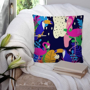 Puede incluir: Una almohada de tiro colorida con un diseño tropical que presenta tucanes y flamencos sobre un fondo azul oscuro. La almohada tiene una variedad de colores verdes, amarillos, rosados y azules.