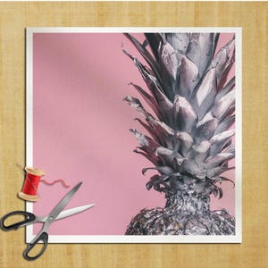 Puede incluir: Una piña plateada sobre un fondo rosa. La piña es una fruta tropical con una parte superior puntiaguda y una piel rugosa y texturizada.