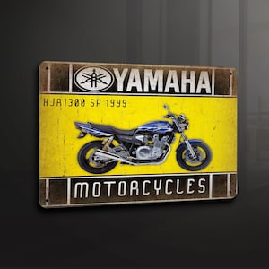 Puede incluir: Una placa de metal amarilla y marrón con el texto "YAMAHA MOTORCYCLES" y una motocicleta Yamaha azul con el texto "HJR1300 SP 1999".