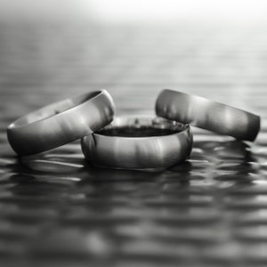May include: Three silver wedding bands stacked on top of each other on a textured surface.