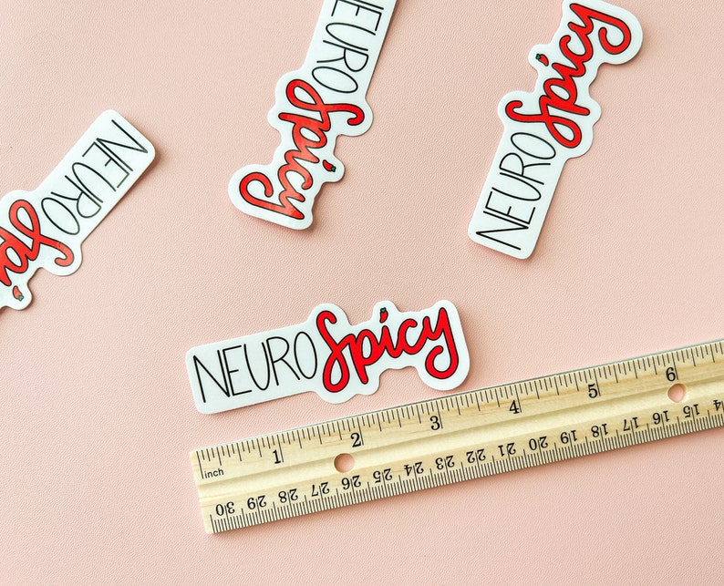 Puede incluir: Cuatro pegatinas blancas con contornos negros y texto rojo que dice "NEURO Spicy". Las pegatinas est&aacute;n sobre una superficie rosa con una regla de madera.