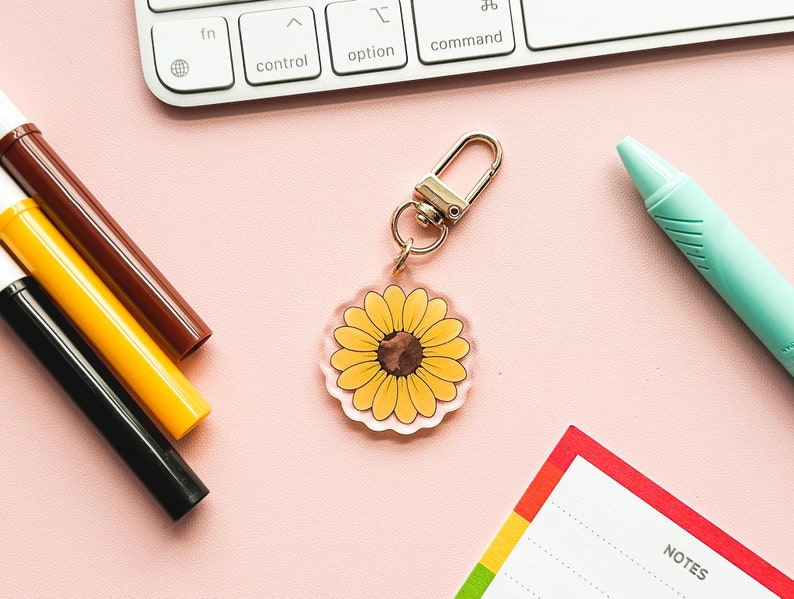 Peut inclure: Un porte-cl&eacute;s en forme de tournesol jaune avec un centre brun. Le porte-cl&eacute;s est en acrylique transparent et poss&egrave;de un anneau en m&eacute;tal argent&eacute;.
