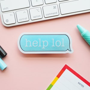 以下が含まれることがあります： ピンクの背景に「help lol」という文字が書かれた青と白のステッカー。画像にはキーボード、青いペン、ノート（「notes」と書いてある）があります。