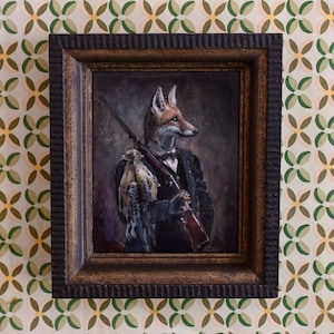 Op de afbeelding: Een ingelijst olieverfschilderij van een vos die een pak draagt en een geweer vasthoudt. De vos houdt een vogel in zijn andere hand. Het schilderij is tegen een donkere achtergrond.