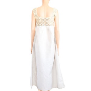 May include: A white linen dress with a crocheted bodice and a flowing skirt. The dress is sleeveless and has a square neckline.