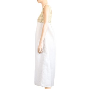 May include: A white linen dress with a crocheted bodice. The dress has a sleeveless design and a midi length. The model is wearing brown heeled sandals.