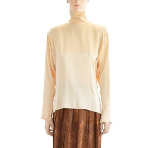 May include: A woman is wearing a light beige turtleneck top and a brown paisley print skirt. She is wearing black heels.