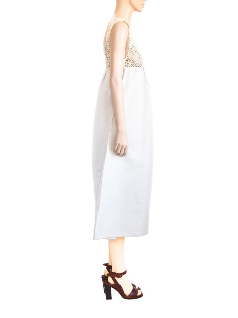 May include: A white maxi dress with a crocheted bodice and a simple, flowing skirt. The dress is worn by a mannequin and has a brown strap sandal on each foot.