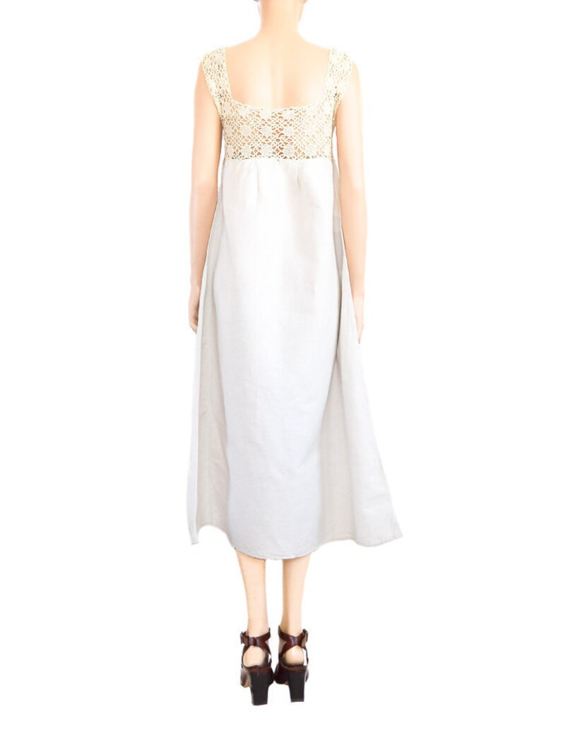 May include: A white linen dress with a crocheted bodice and a flowing skirt. The dress is sleeveless and has a square neckline.