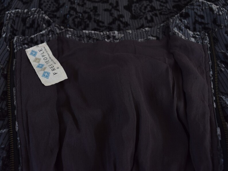 May include: A black velvet dress with a floral pattern and a zipper closure. The dress has a Free People tag attached to the inside.