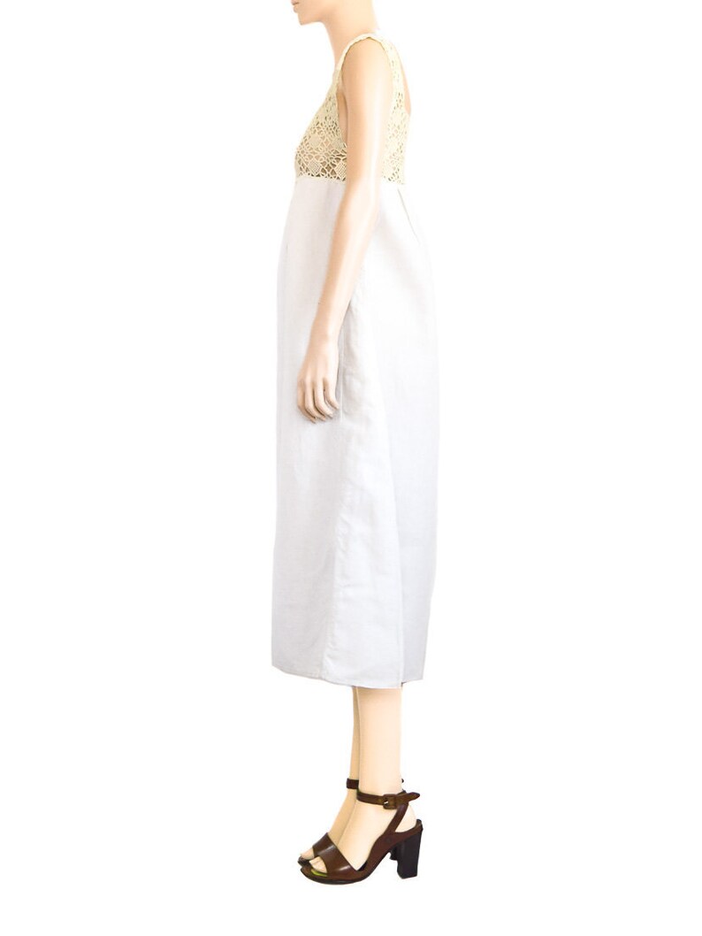 May include: A white linen dress with a crocheted bodice. The dress has a sleeveless design and a midi length. The model is wearing brown heeled sandals.
