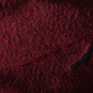 May include: Close-up of a dark red fabric with a textured weave. The fabric has a subtle sheen and a diagonal seam.