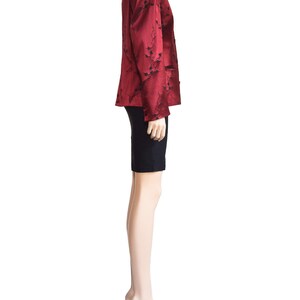 May include: A red satin blazer with a black floral pattern. The blazer has a mandarin collar and long sleeves. The model is wearing a black skirt and black heels.