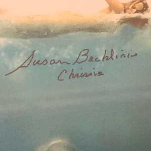 Puede incluir: Pintura artística de una nadadora en el agua. El brazo de la nadadora está extendido y la cabeza es visible. El agua es una mezcla de azul y blanco, con el cielo al fondo. La firma del artista, "Susan Backlinis Chrisie", es visible.
