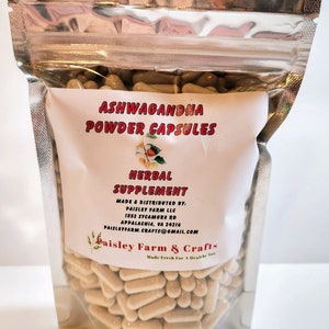 May include: A clear plastic bag filled with beige capsules labeled "Ashwagandha Powder Capsules" and "Herbal Supplement". The bag is sealed with a silver zipper. The label also includes the company name "Paisley Farm & Crafts" and contact information.