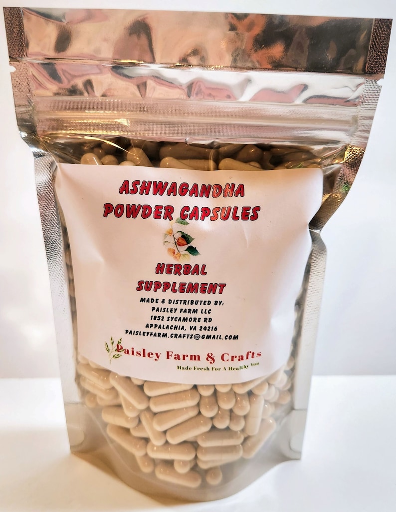 May include: A clear plastic bag filled with beige capsules labeled "Ashwagandha Powder Capsules" and "Herbal Supplement". The bag is sealed with a silver zipper. The label also includes the company name "Paisley Farm & Crafts" and contact information.