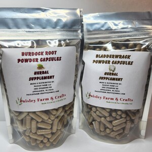 May include: Two clear plastic bags filled with brown capsules. The bag on the left has a label that reads "Burdock Root Powder Capsules Herbal Supplement" and the bag on the right has a label that reads "Bladderwrack Powder Capsules Herbal Supplement". Both bags have the same logo, "Paisley Farm & Crafts Made Fresh for a Healthy You".