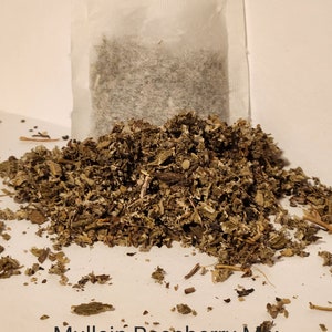 May include: A white tea bag filled with loose leaf tea sits on a pile of dried herbs labelled "Mullein Raspberry Mix".